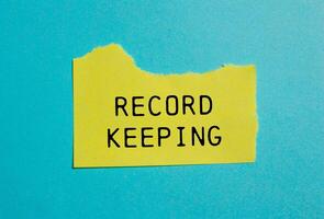 Record keeping message written on ripped torn yellow paper with blue background. Conceptual record keeping symbol. Copy space. photo