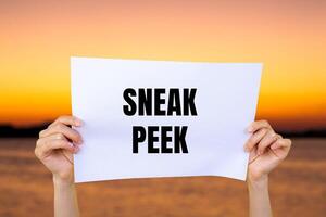 Sneak peek message written on white paper with blurry lake background. Conceptual sneak peek symbol. Copy space. photo