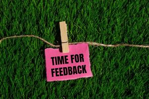 Time for feedback message written on ripped torn pink paper piece with green grass background. Conceptual time for feedback symbol. Copy space. photo