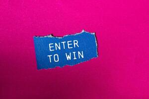 Enter to win message written on ripped blue torn paper piece on pink background. Conceptual enter to win symbol. Copy space. photo