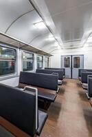 interior of an cheap empty train car with simple bench-style seating. The car features metal luggage racks above the windows, a clean, minimalist design, and a bright, neutral color scheme. photo
