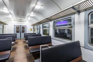 interior of an cheap empty train car with simple bench-style seating. The car features metal luggage racks above the windows, a clean, minimalist design, and a bright, neutral color scheme. photo