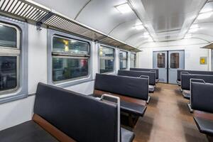interior of an cheap empty train car with simple bench-style seating. The car features metal luggage racks above the windows, a clean, minimalist design, and a bright, neutral color scheme. photo