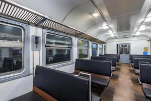 interior of an cheap empty train car with simple bench-style seating. The car features metal luggage racks above the windows, a clean, minimalist design, and a bright, neutral color scheme. photo