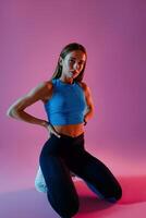 Attractive fitness woman wearing sportswear is kneeling and posing on studio background photo