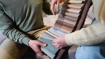A man and woman choosing upholstery fabric color and texture from various colorful samples for sofa in a store, close up video