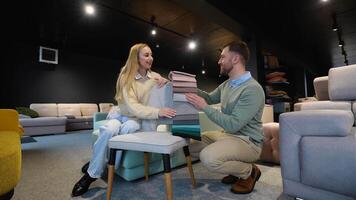 Just married couple choosing upholstery fabric color and texture from various colorful samples for armchair in a store video