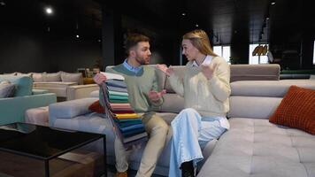 A man and woman choosing upholstery fabric color and texture from various colorful samples for sofa in a store video