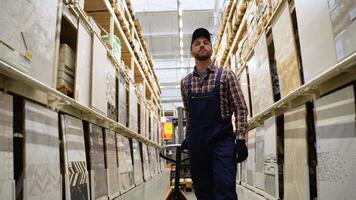 Warehouse worker is working with hand pallet truck or pallet jack and cargo pallet in a construction store in tile section video