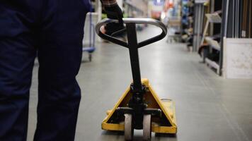 A worker in a warehouse or hardware store uses a hand pallet stacker to transport pallets video