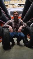A man in a tire store with two new tires for car. Vertical video
