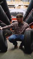 A man in a tire store with two new tires for car. Vertical video