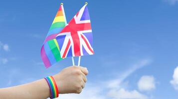 Cut out of hand holding both the LGBT flag and the United Kingdom flag, set against blue sky background with clipping paths. The symbolizing unity, diversity, and inclusion. photo