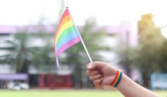 Cut out of hand holding the LGBT flag, set against set against blurred background. The colorful flag stands out prominently, representing pride, the celebration of diversity and inclusion. photo