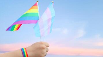 Cut out of hand holding both the LGBT flag and the LGBTQIA flag, set against blue sky background with clipping paths. The symbolizing unity, diversity, and inclusion. photo