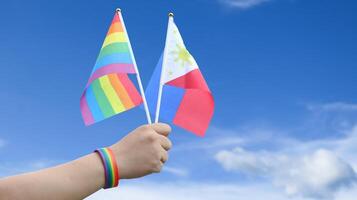 Cut out of hand holding both the LGBT flag and the Philippines flag, set against blue sky background with clipping paths. The symbolizing unity, diversity, and inclusion. photo