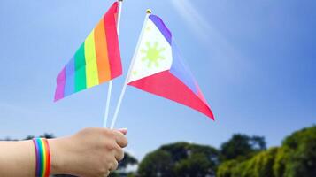 Cut out of hand holding both the LGBT flag and the Philippines flag, set against blue sky background with clipping paths. The symbolizing unity, diversity, and inclusion. photo