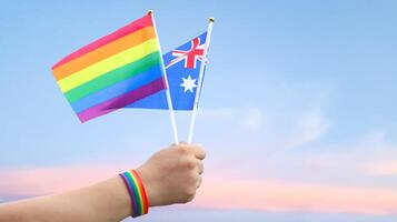Cut out of hand holding both the LGBT flag and the Australia flag, set against blue sky background with clipping paths. The symbolizing unity, diversity, and inclusion. photo