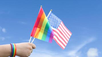 Cut out of hand holding both the LGBT flag and the American flag, set against blue sky background with clipping paths. The symbolizing unity, diversity, and inclusion. photo