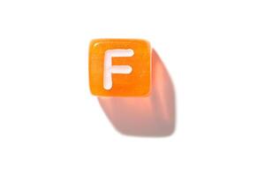 Orange cube with white letter f casting shadow on white background. photo