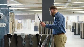A man chooses a shower mixer in luxury plumbing store. Buyer checks the faucet before purchasing video