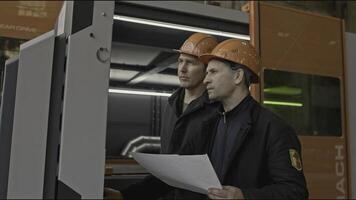 Workers look at paper and industrial computer. Stock clip. Checking settings of industrial computer device and its readings. Working with computer of industrial machine photo