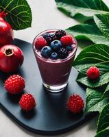 A smoothie is garnished with berries on a dark surface Surrounding it are leaves and pomegranates. photo