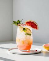 A glass of pink grapefruit and mint cocktail on a white table photo