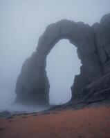 A large rock arch in the fog on a beach photo