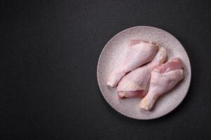 Raw chicken legs with salt, spices and herbs on a dark concrete background photo