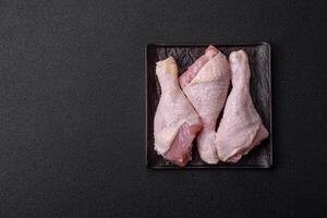 Raw chicken legs with salt, spices and herbs on a dark concrete background photo