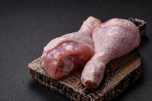 Raw chicken legs with salt, spices and herbs on a dark concrete background photo