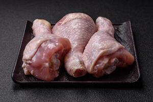 Raw chicken legs with salt, spices and herbs on a dark concrete background photo