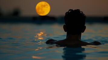 As the moon rises it casts a soft glow over the bather creating a tranquil atmosphere photo