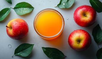 A glass of apple juice is poured into a glass bowl next to two apples. The apples are red and shiny, and the bowl is filled with the juice. Concept of freshness and health, as the apples photo