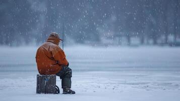 A lone ice fisherman sitting on a wooden stool patiently waiting for a bite as the snow falls gently around him on the frozen lake photo