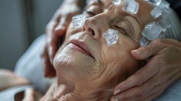 A the gently rubs ice cubes over the face and neck of an older woman using cryotherapy techniques to improve circulation and reduce wrinkles photo