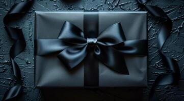 A black box with a bow on top of it. The box is wrapped in black paper and has a ribbon around it. photo
