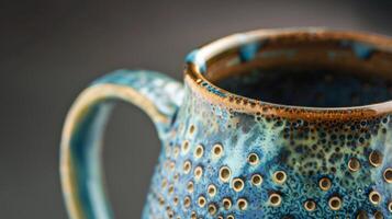 A closeup of a handmade mug textured with tiny raised dots and adorned with a dripping glaze in shades of turquoise and midnight blue photo