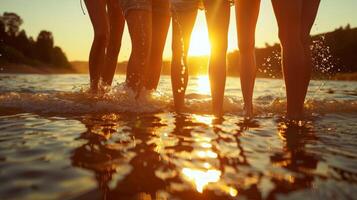 The sun setting behind a group of friends standing kneedeep in a lake arms linked as they brace themselves against the cold water photo