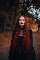 Mysterious gothic girl in dark witch clothes on autumn forest background, halloween photo