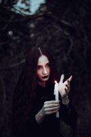 Witch in a black costume holds candle in a dark forest, mysterious atmosphere, ritual, halloween photo