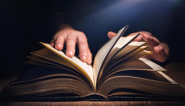 A close-up of hands flipping through the pages of an open book under dramatic lighting, creating a focused reading atmosphere. photo