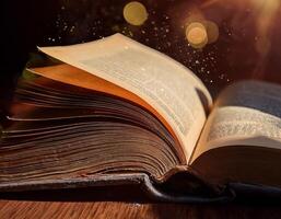 An old book with yellowed pages open on a table, illuminated by warm light and glowing dust particles in the air. photo