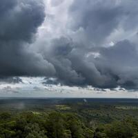 Moody view of dark storm clouds gathering over a vast green forest landscape, creating a dramatic and atmospheric scene. photo
