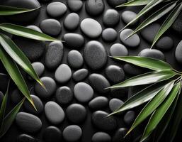A collection of smooth black pebbles arranged with green bamboo leaves, creating a tranquil and natural spa-like composition. photo