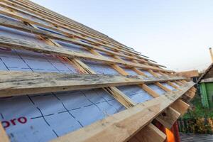 lose-up of a wooden roof frame during construction. The wooden planks are arranged in a grid pattern and supported by beams, creating a sturdy foundation for the roof. photo