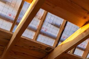 lose-up of a wooden roof frame during construction. The wooden planks are arranged in a grid pattern and supported by beams, creating a sturdy foundation for the roof. photo