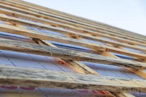 lose-up of a wooden roof frame during construction. The wooden planks are arranged in a grid pattern and supported by beams, creating a sturdy foundation for the roof. photo