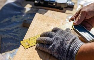 Yellow ruler placed on a wooden beam. Tools are being used to measure and mark the wooden beam for cutting or construction. The close-up view of the tools and the wooden beam. photo